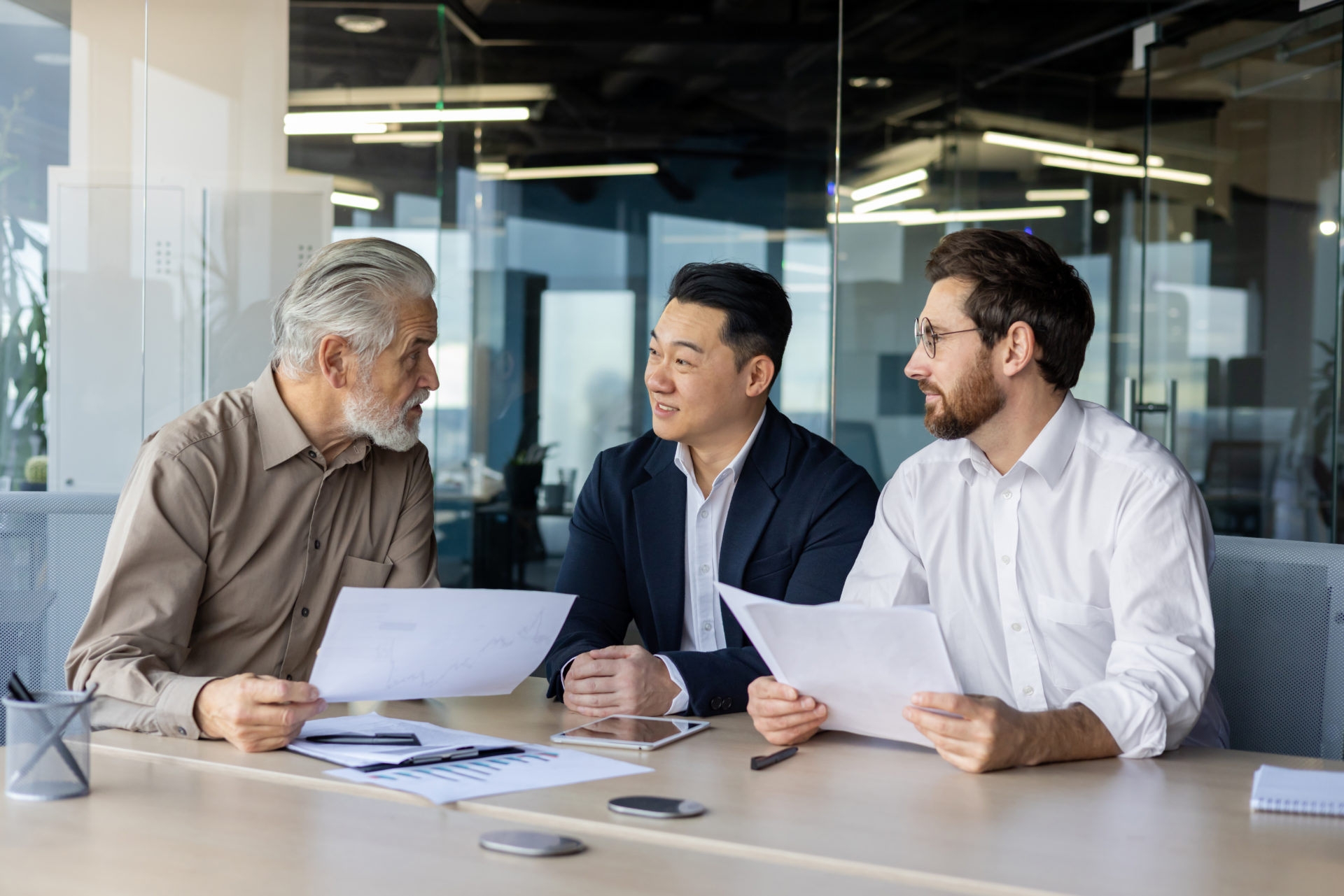Group of businessmen sitting in the office at the table, holding work documents, holding a work meeting, discussing important issues.